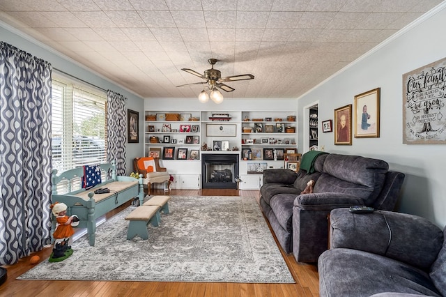 living area featuring built in shelves, a fireplace, light wood-style flooring, and crown molding