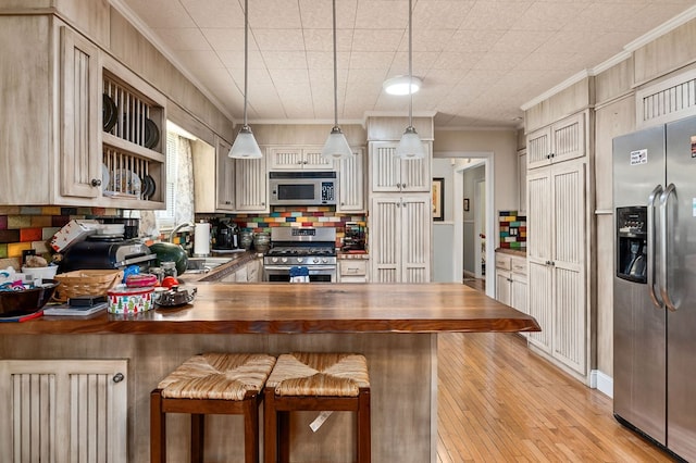 kitchen featuring a breakfast bar area, pendant lighting, a peninsula, stainless steel appliances, and wooden counters