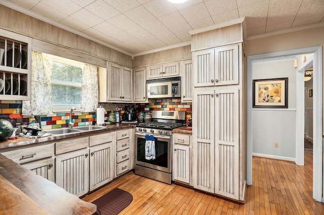 kitchen with light wood finished floors, appliances with stainless steel finishes, a sink, and ornamental molding