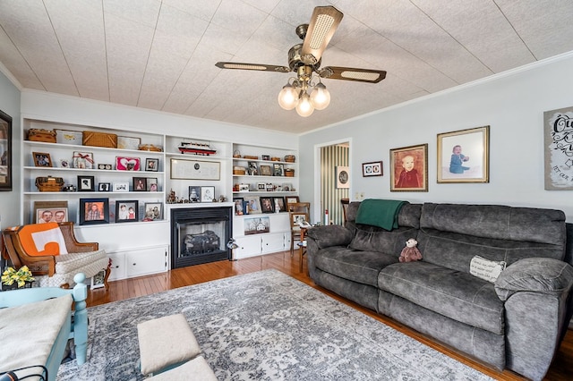 living area featuring a fireplace, wood finished floors, a ceiling fan, and crown molding