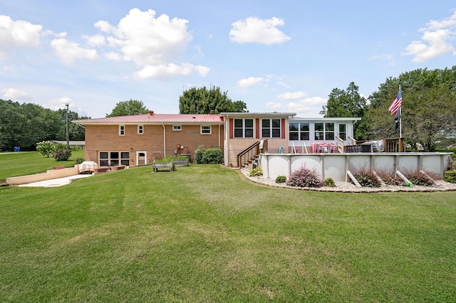 rear view of property featuring brick siding, a sunroom, a yard, stairway, and an outdoor pool