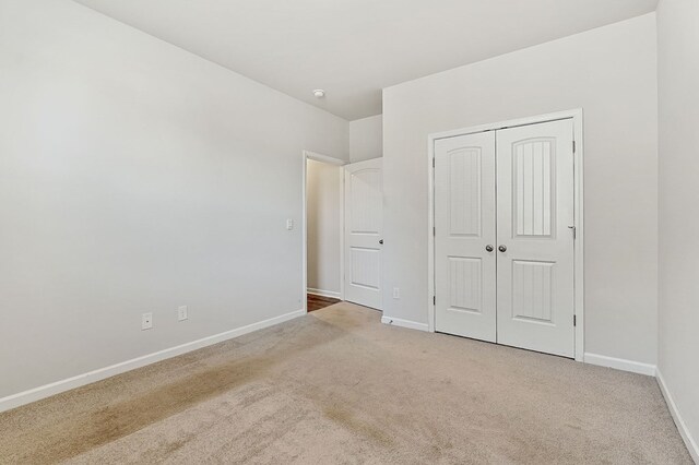 unfurnished bedroom featuring a closet, light colored carpet, and baseboards