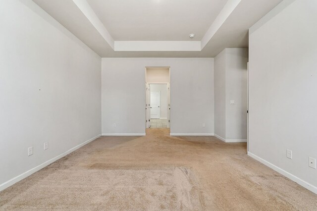 empty room featuring a tray ceiling, light colored carpet, and baseboards