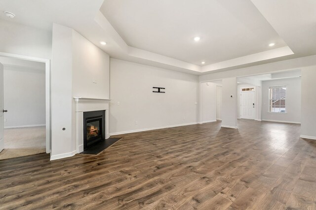 unfurnished living room featuring baseboards, dark wood-style floors, a fireplace with flush hearth, a tray ceiling, and recessed lighting