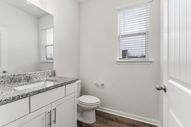 half bath with baseboards, vanity, toilet, and wood finished floors