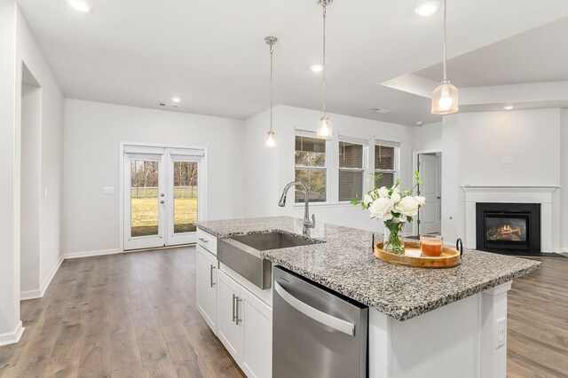 kitchen with decorative light fixtures, stainless steel dishwasher, a kitchen island with sink, white cabinets, and a sink