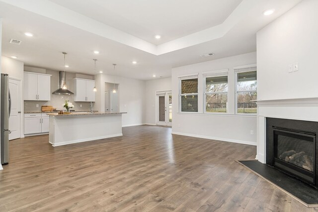 unfurnished living room with a glass covered fireplace, visible vents, baseboards, and wood finished floors