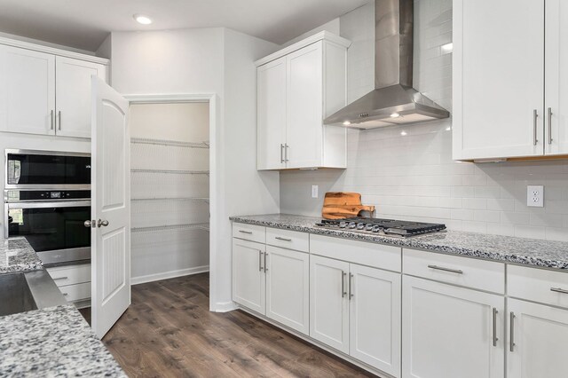 kitchen featuring stainless steel appliances, white cabinets, wall chimney range hood, and light stone countertops