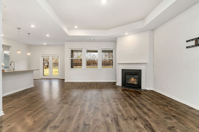 unfurnished living room featuring baseboards, a raised ceiling, a glass covered fireplace, dark wood-style floors, and recessed lighting