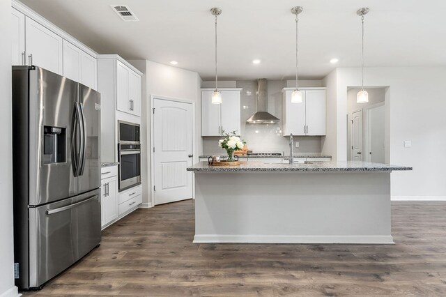 kitchen featuring visible vents, white cabinets, appliances with stainless steel finishes, wall chimney exhaust hood, and a center island with sink