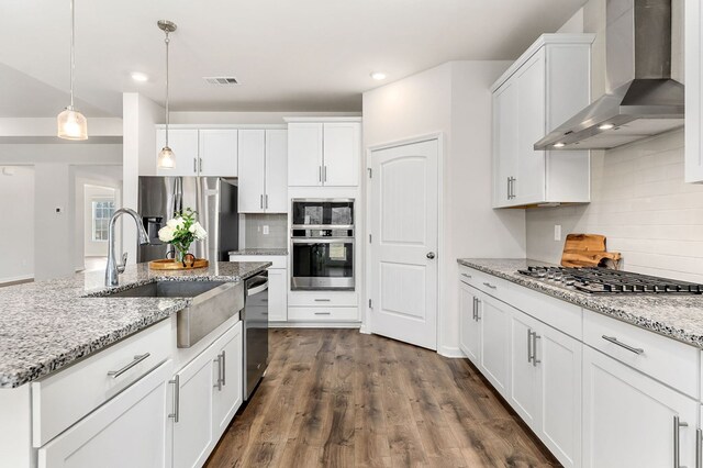 kitchen featuring white cabinetry, wall chimney exhaust hood, appliances with stainless steel finishes, and decorative light fixtures