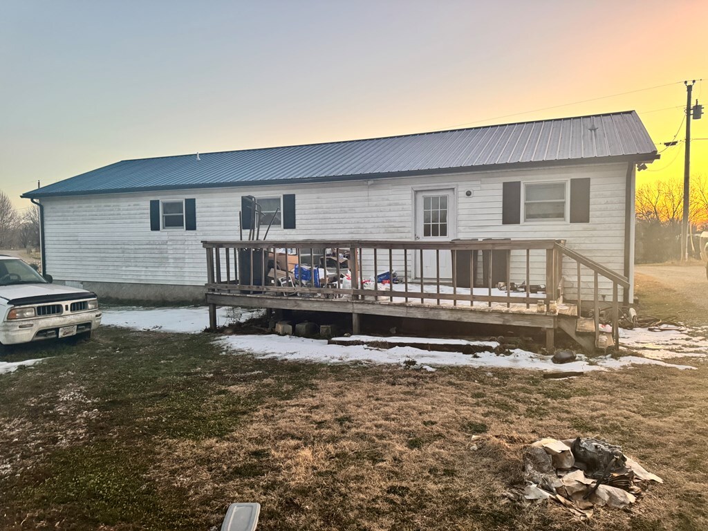 back of house at dusk with a wooden deck, metal roof, and a yard