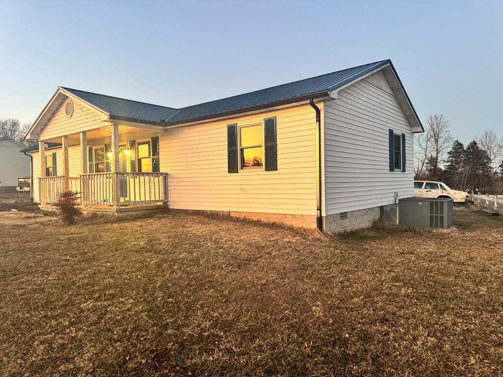 view of side of property with a lawn, metal roof, crawl space, covered porch, and central air condition unit