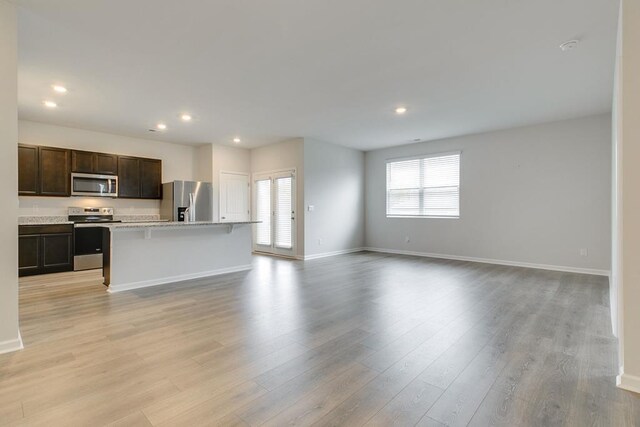 kitchen featuring a breakfast bar area, appliances with stainless steel finishes, open floor plan, dark brown cabinets, and an island with sink