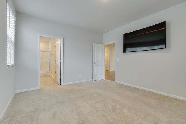 unfurnished bedroom with baseboards, connected bathroom, and light colored carpet