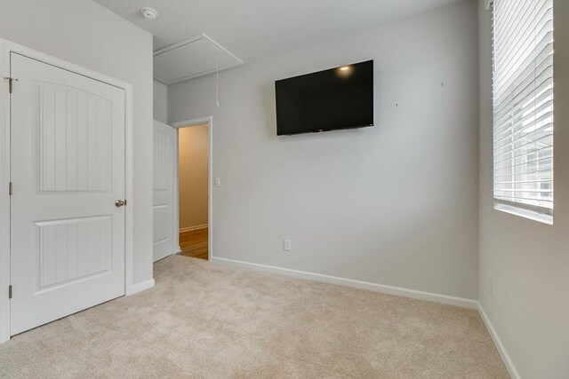 unfurnished bedroom featuring light carpet, attic access, and baseboards