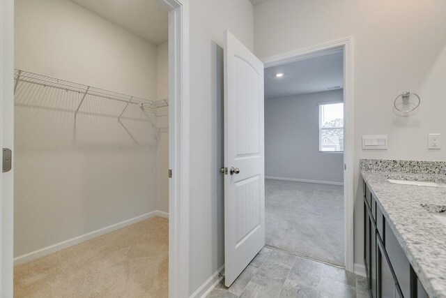 full bath with a spacious closet, double vanity, and baseboards