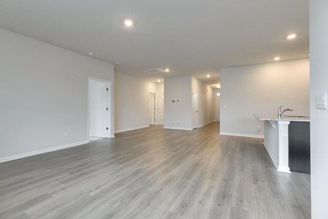 unfurnished living room featuring a sink, light wood-style flooring, and baseboards