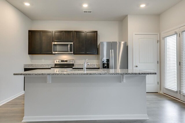 kitchen featuring appliances with stainless steel finishes, a kitchen island with sink, and light stone countertops