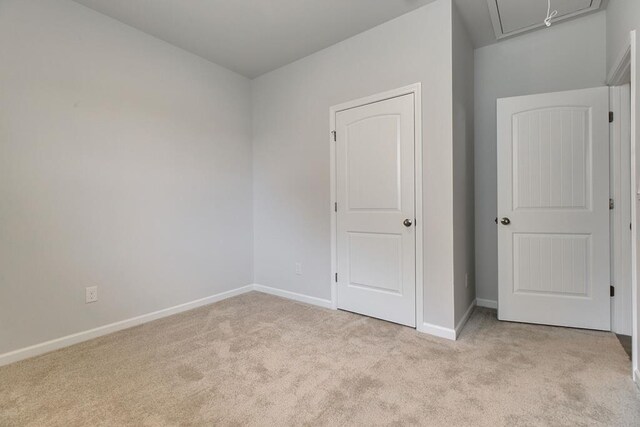 unfurnished bedroom with light carpet, attic access, and baseboards