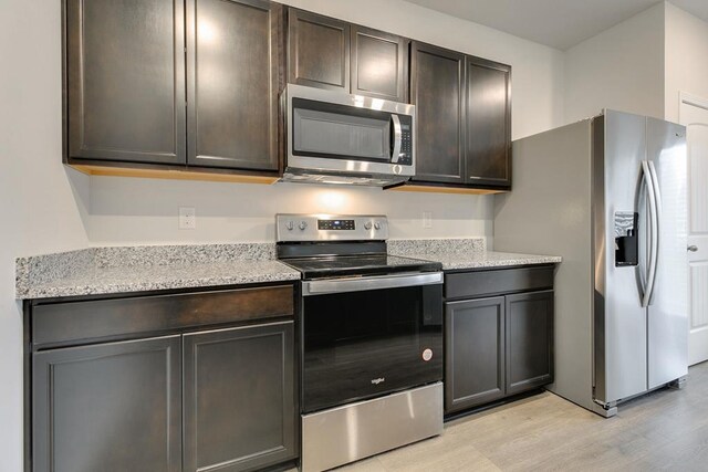 kitchen with appliances with stainless steel finishes, light wood-type flooring, dark brown cabinets, and light stone countertops