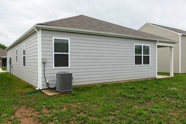 view of home's exterior with cooling unit, roof with shingles, and a yard