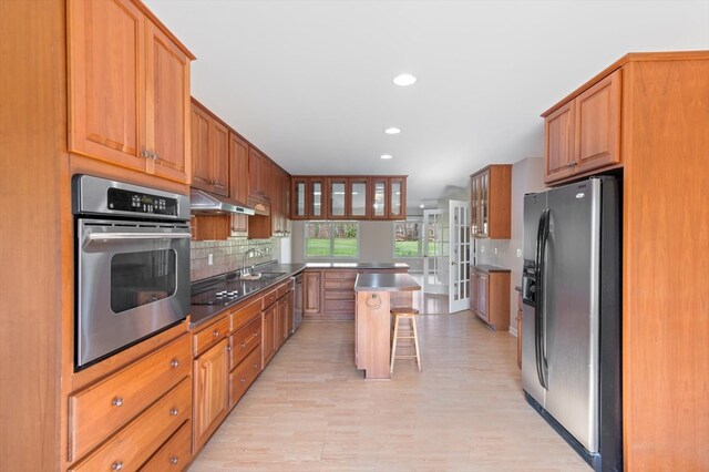 kitchen featuring dark countertops, glass insert cabinets, a center island, stainless steel appliances, and a kitchen bar