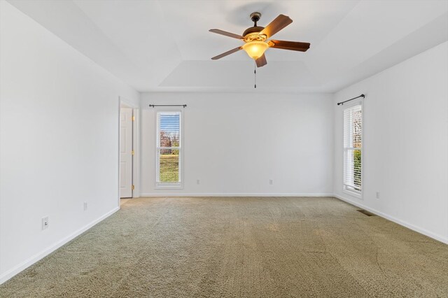 carpeted empty room with ceiling fan, a raised ceiling, and baseboards