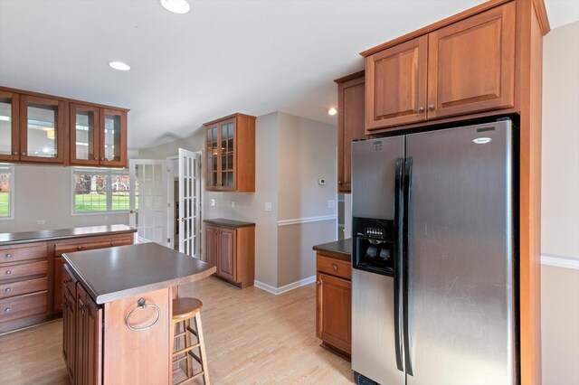 kitchen with a breakfast bar area, dark countertops, glass insert cabinets, a kitchen island, and stainless steel fridge