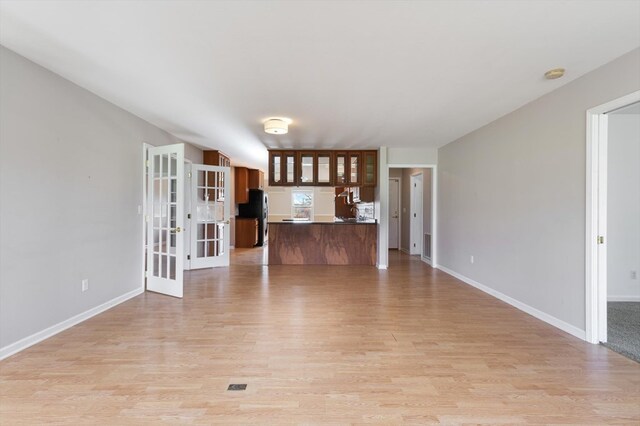 unfurnished living room featuring light wood-type flooring, french doors, and baseboards