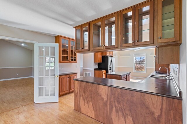 kitchen with brown cabinets, dark countertops, visible vents, glass insert cabinets, and a sink