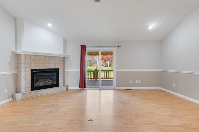 unfurnished living room featuring visible vents, baseboards, a tiled fireplace, vaulted ceiling, and light wood-type flooring