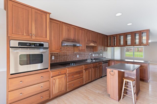 kitchen featuring a breakfast bar area, under cabinet range hood, stainless steel appliances, a center island, and glass insert cabinets