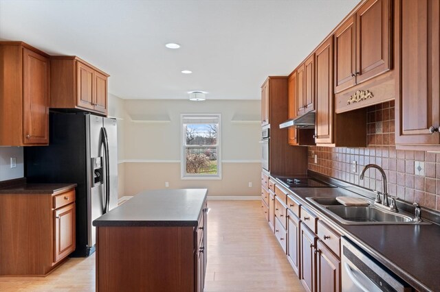 kitchen with dark countertops, a kitchen island, appliances with stainless steel finishes, under cabinet range hood, and a sink