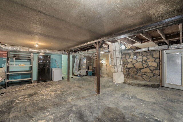 unfinished basement featuring heating unit, a textured ceiling, and freestanding refrigerator