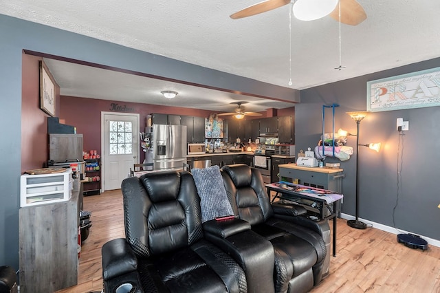 living room with light wood-style floors, baseboards, a ceiling fan, and a textured ceiling