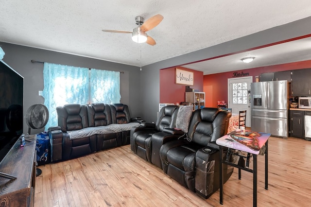 living room with ceiling fan, light wood-style flooring, and a textured ceiling