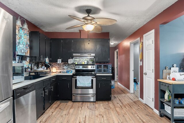 kitchen featuring light wood-type flooring, appliances with stainless steel finishes, light countertops, and dark cabinets