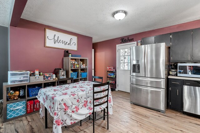 kitchen featuring stainless steel appliances, dark cabinetry, light countertops, and light wood-style floors