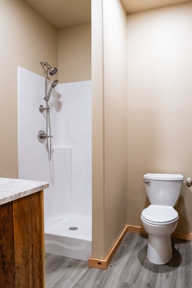 bathroom with a stall shower, baseboards, toilet, wood finished floors, and vanity