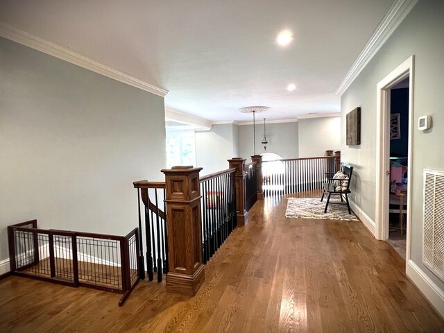 corridor featuring baseboards, ornamental molding, wood finished floors, and an upstairs landing