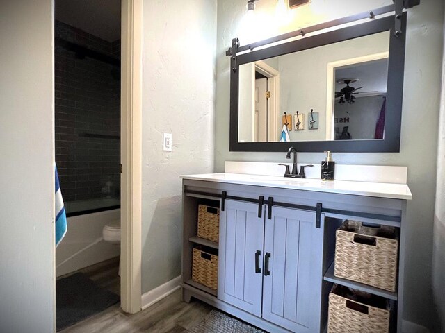 full bathroom featuring toilet, enclosed tub / shower combo, vanity, wood finished floors, and baseboards