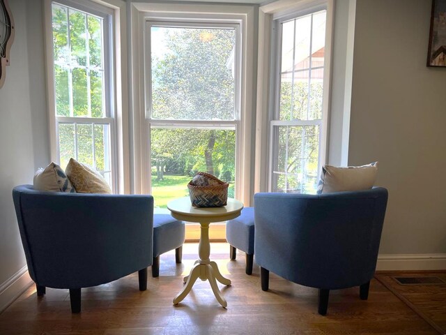 sitting room with baseboards, plenty of natural light, visible vents, and wood finished floors