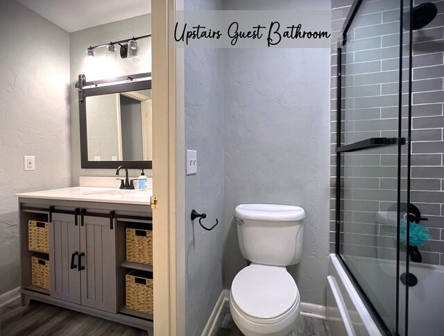 bathroom featuring a textured wall, toilet, enclosed tub / shower combo, vanity, and wood finished floors