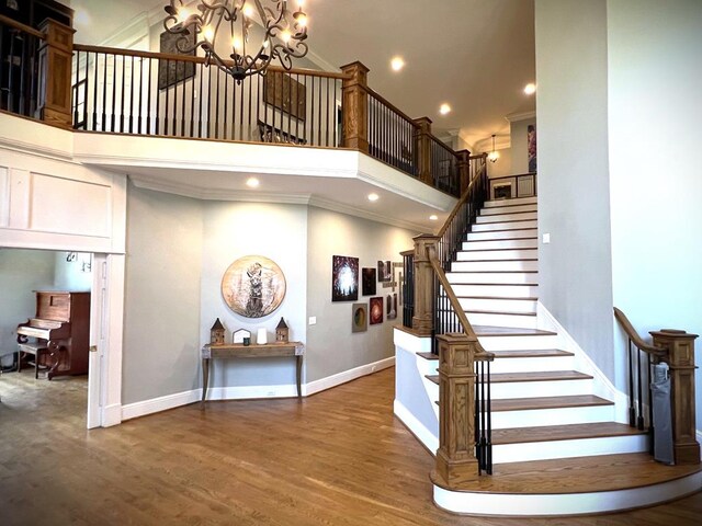 staircase featuring a notable chandelier, recessed lighting, a towering ceiling, wood finished floors, and baseboards