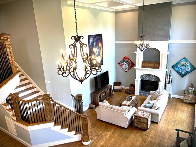 living area featuring wood finished floors, a large fireplace, a high ceiling, and an inviting chandelier