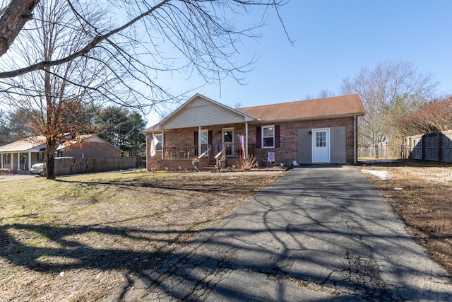 view of front facade with brick siding, aphalt driveway, fence, a porch, and a front yard