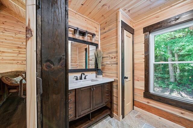 bathroom with stone tile floors, wood walls, wood ceiling, vanity, and plenty of natural light