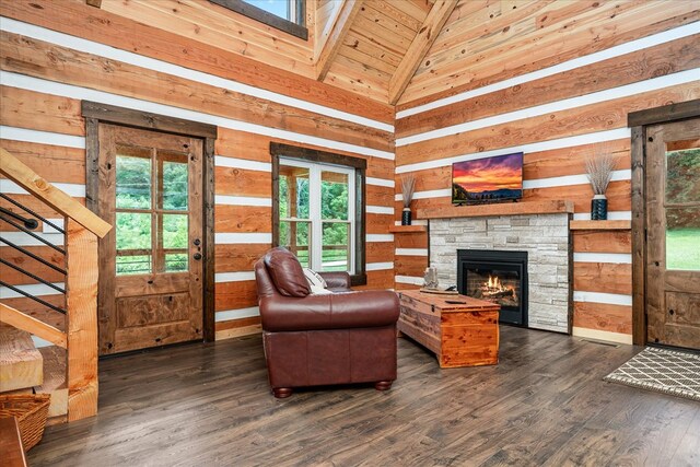 living area featuring dark wood finished floors, stairway, wood walls, a stone fireplace, and high vaulted ceiling