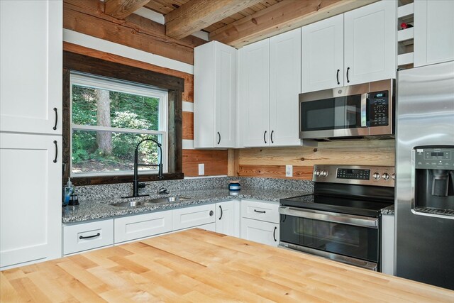 kitchen with light stone counters, stainless steel appliances, a sink, white cabinetry, and beam ceiling